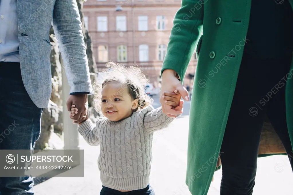 Happy girl walking with midsection of parents in city