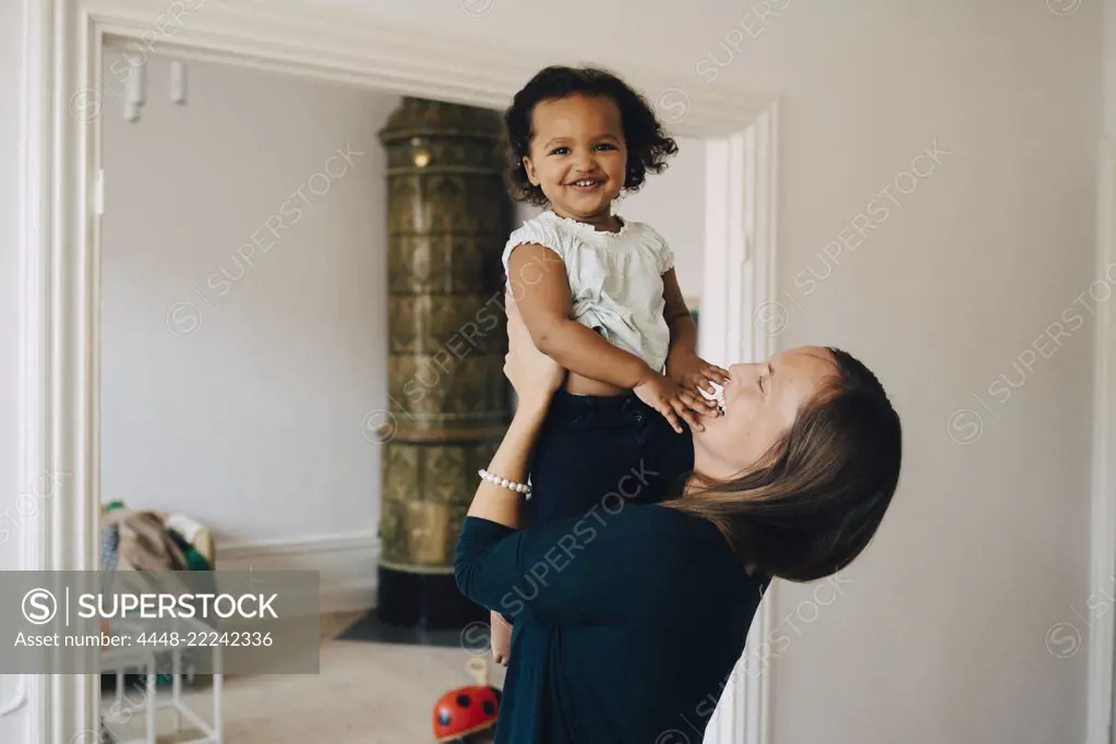 Happy mother holding daughter while standing at home