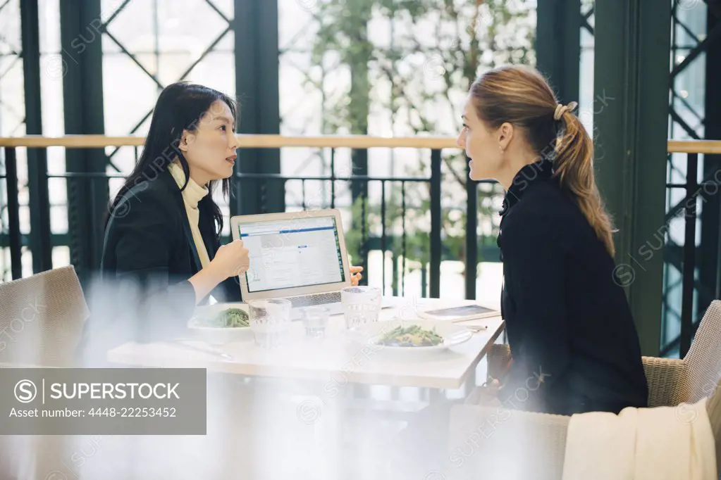 Confident multi-ethnic female business colleagues discussing over laptop at cafeteria