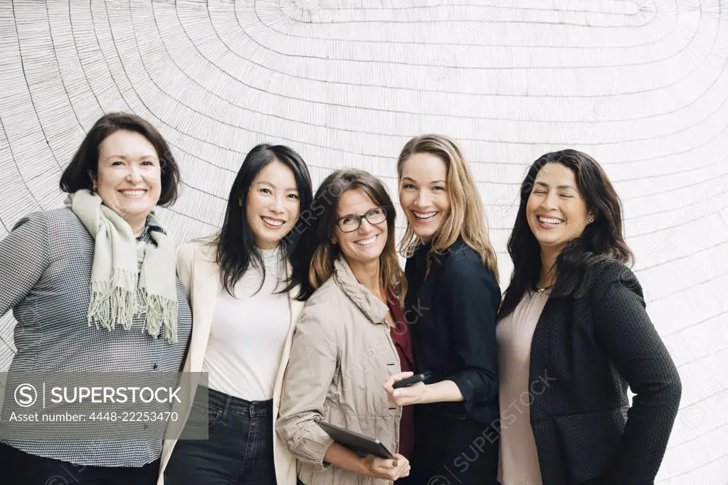 Portrait of smiling multi-ethnic businesswomen standing against wall at workplace