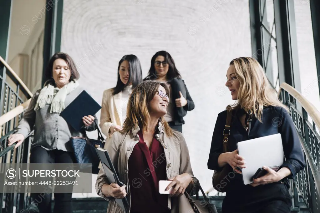 Low angle view of multi-ethnic female entrepreneurs moving down on staircase in office