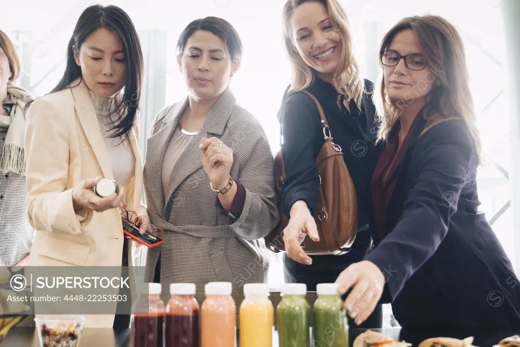 Multi-ethnic businesswomen looking at food and drink on table in event