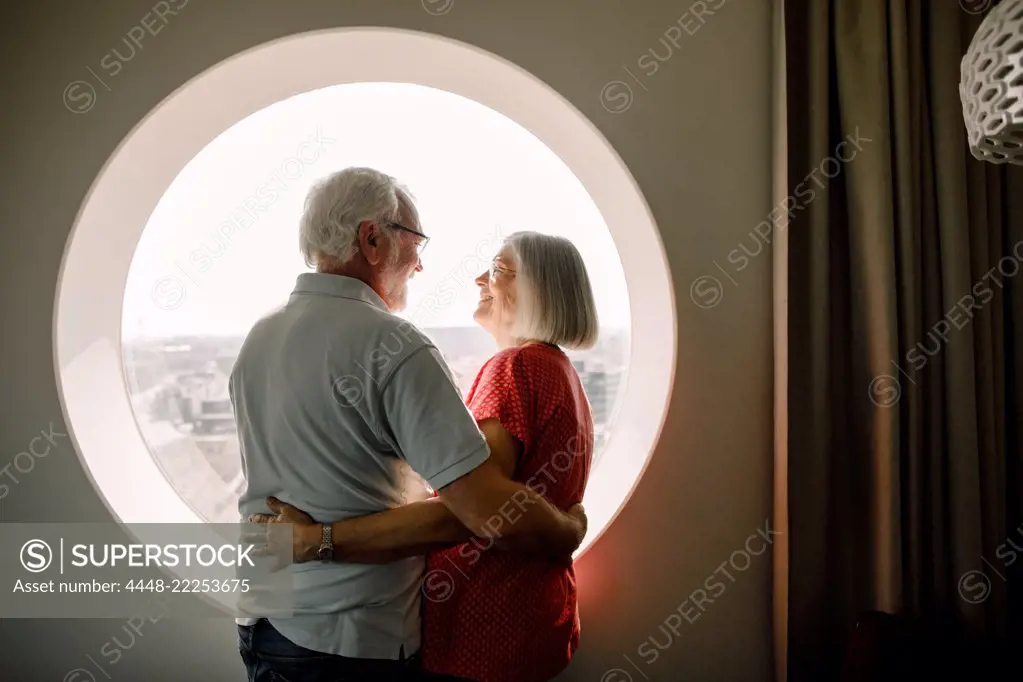 Senior couple embracing while standing by window in hotel room