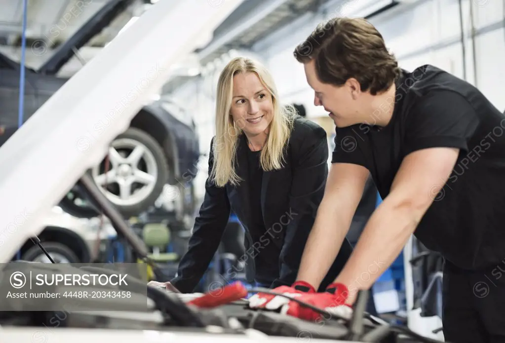 Male mechanic discussing with female customer while repairing car engine at workshop