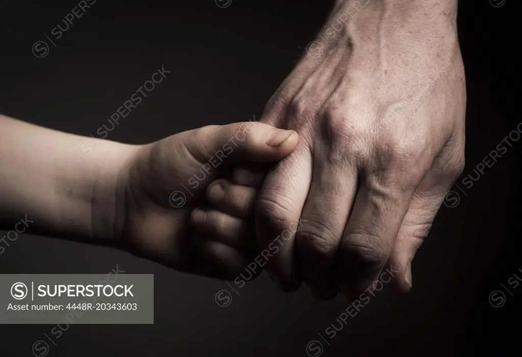 Cropped image of father and son holding hands against black background