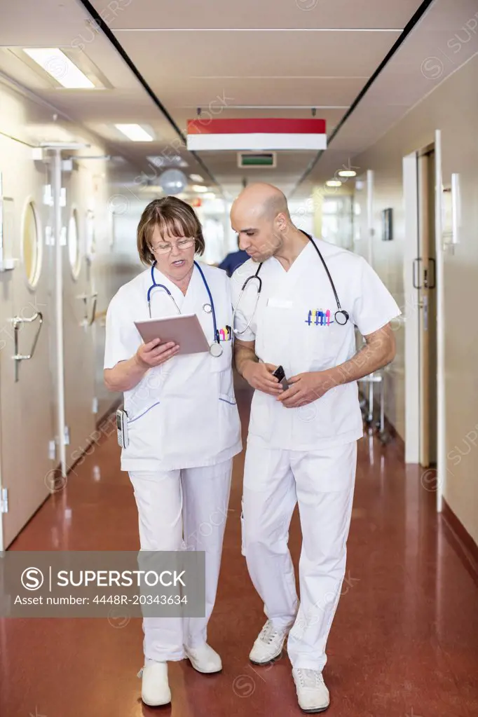 Male and female doctors using digital tablet while walking in hospital corridor