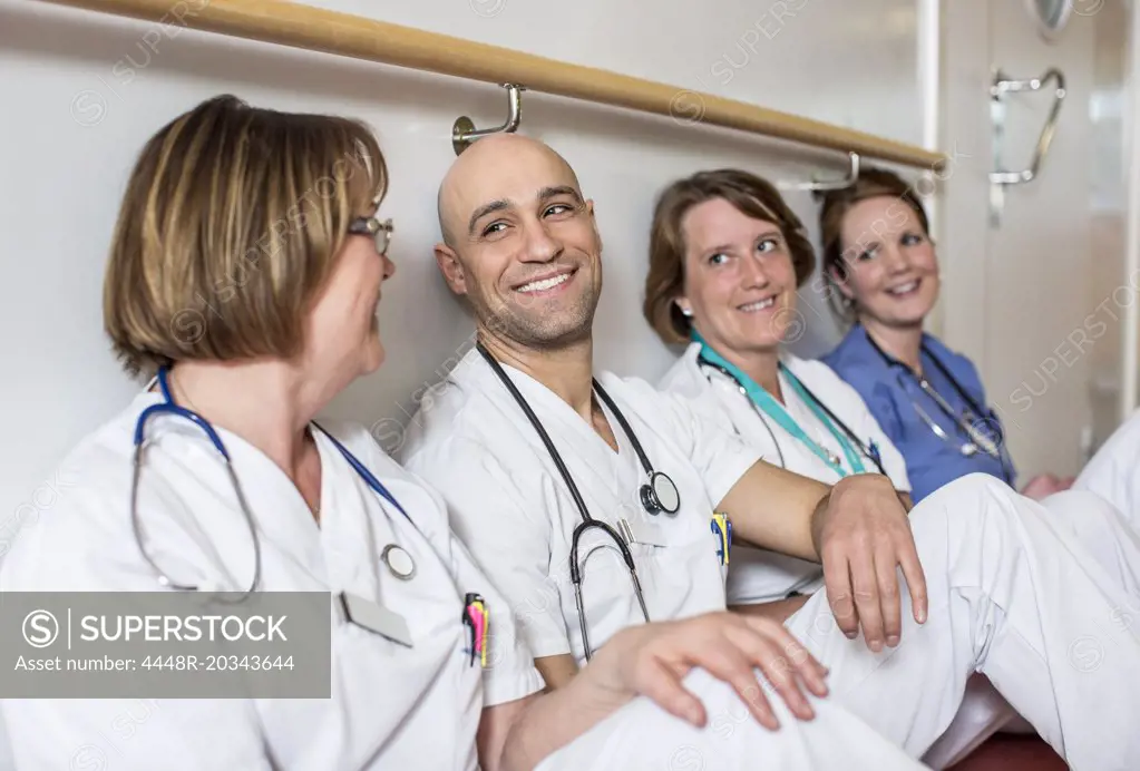 Happy male doctor and female colleagues leaning together on wall in hospital