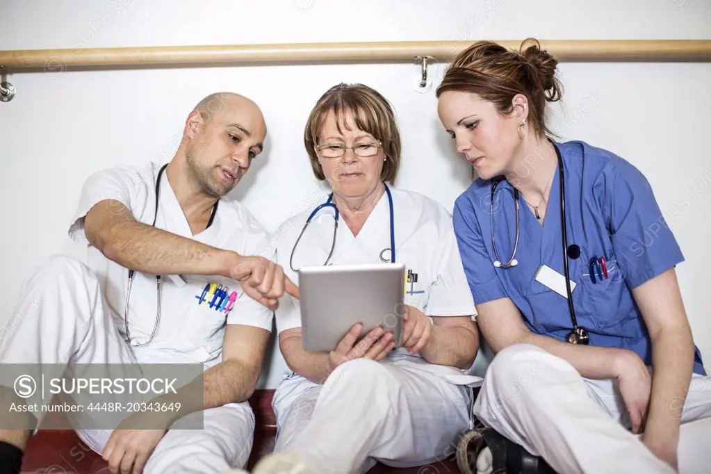 Doctors using digital tablet while leaning on wall in hospital