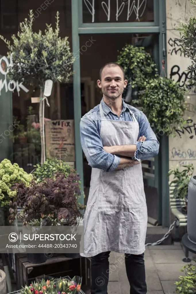 Portrait of confident male florist standing arms crossed outside flower shop