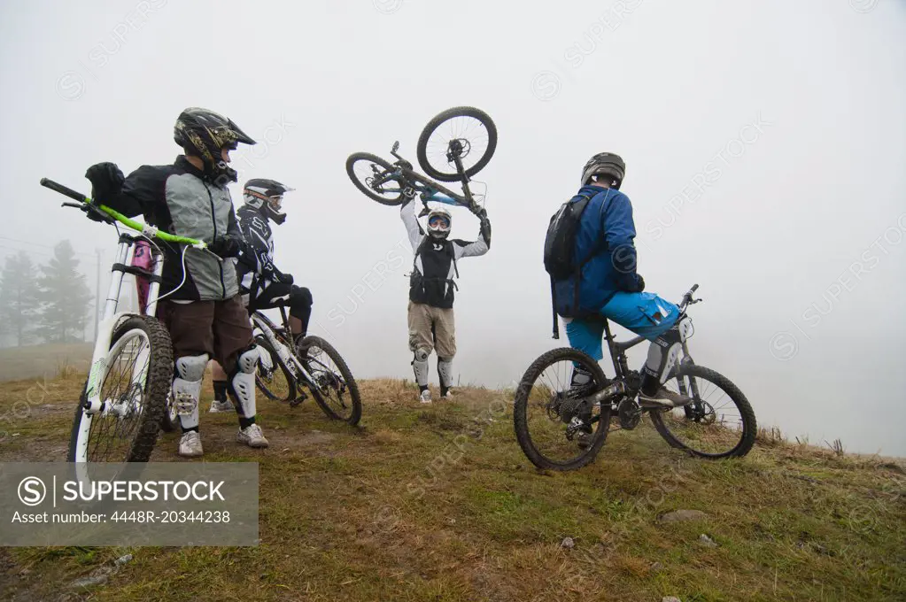 Friends looking at man picking up bicycle on mountain