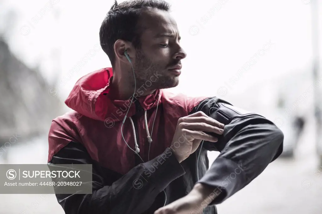 Sporty man adjusting arm band while listening to music