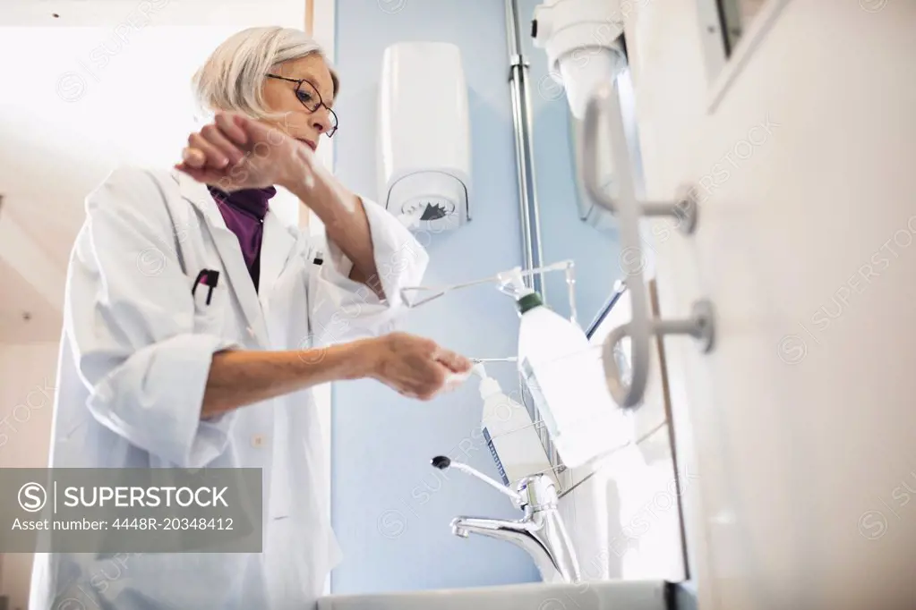 Low angle view of senior female doctor using soap dispenser to wash hands in bathroom