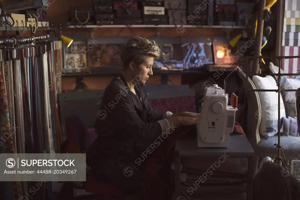 Side view of female fashion designer using sewing machine in studio