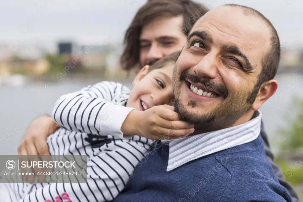 Happy son playing with gay man's beards outdoors