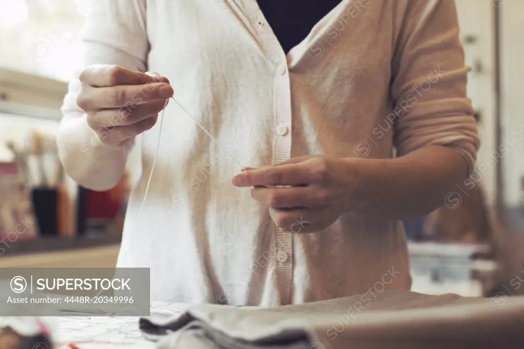 Midsection of woman threading needle while standing at table