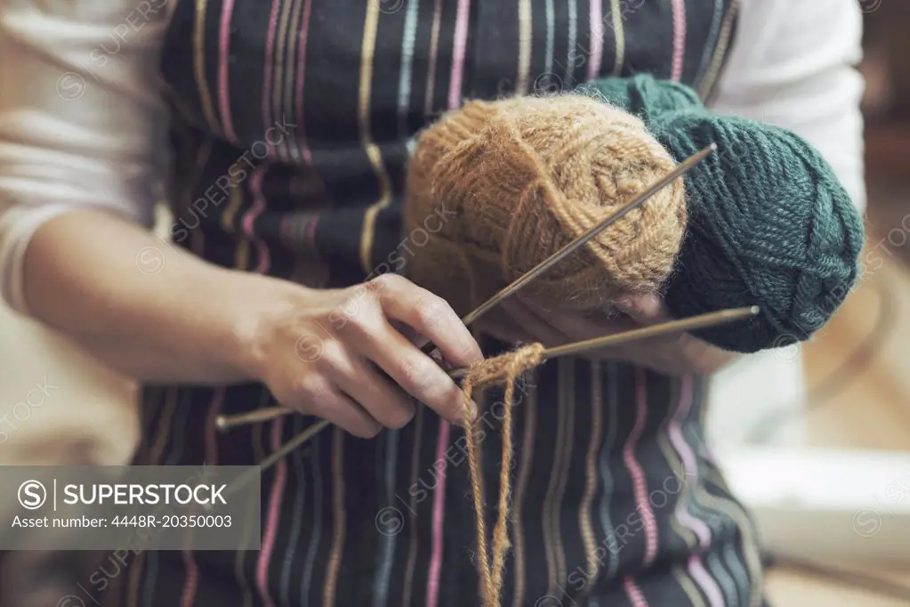 Midsection of woman holding knitting tools at home