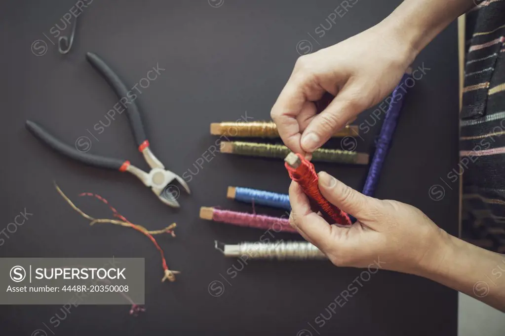 Directly above shot of woman rolling wire on spool at table