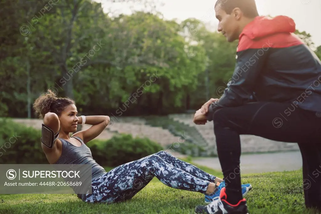 Man kneeling and looking at woman doing sit-ups on field