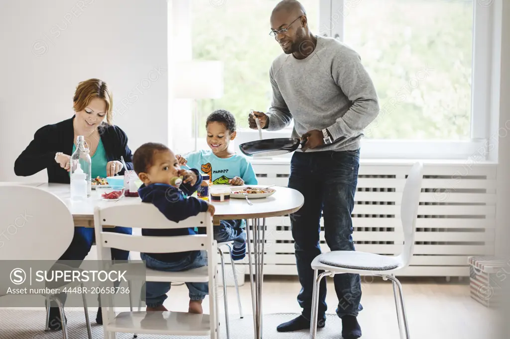 Man serving food to family at dining table in house