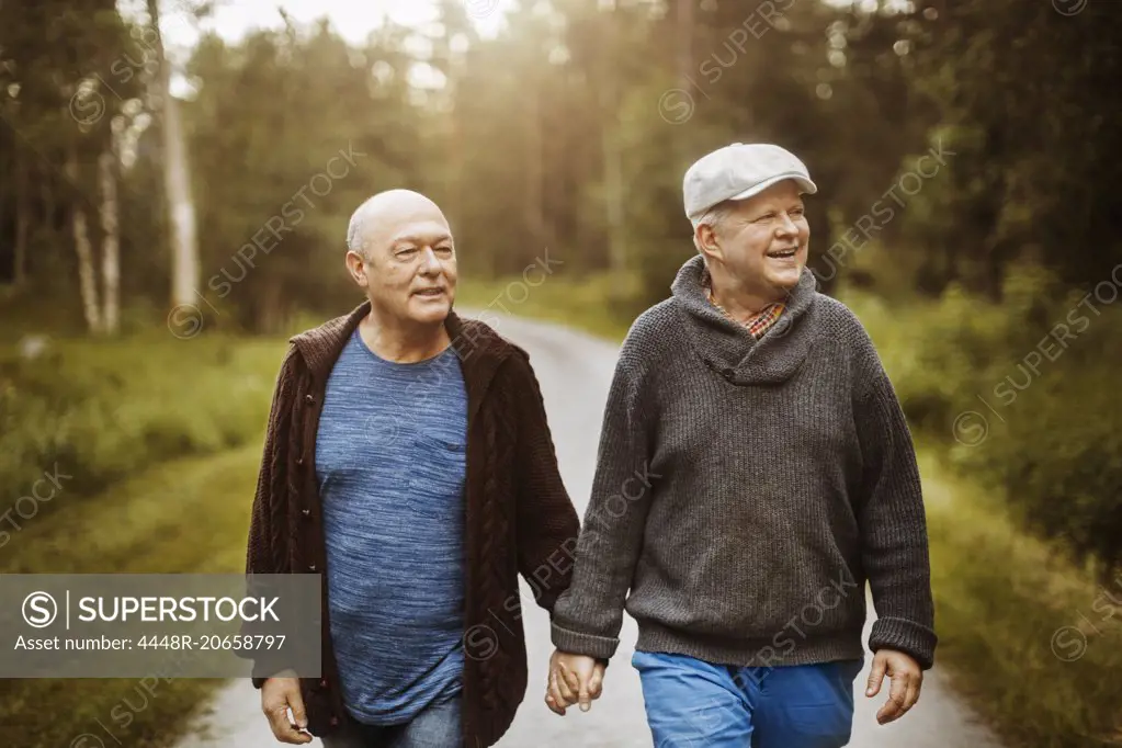 Happy gay couple looking away while walking on road amidst trees