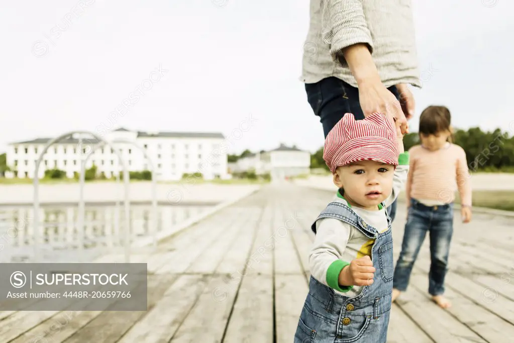 Portrait of baby girl standing with family on pier at beach against clear sky