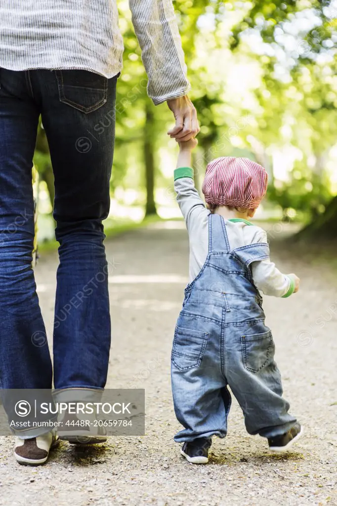 Rear view of baby girl holding mother's hand while walking on dirt road