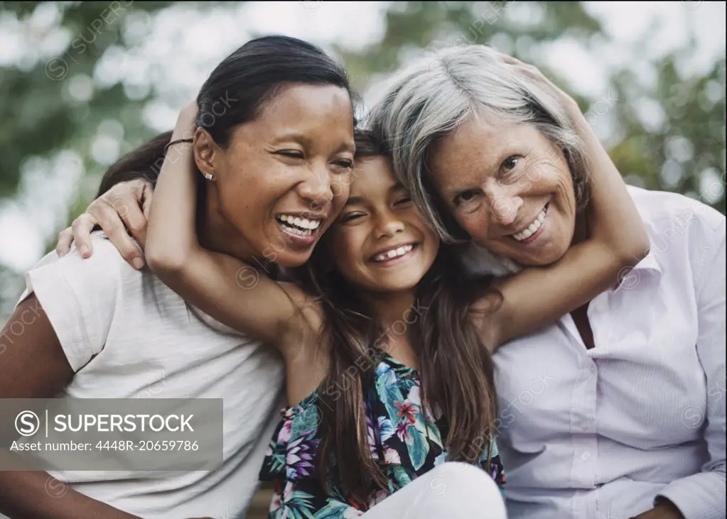 Portrait of happy girl embracing mother and grandmother at yard