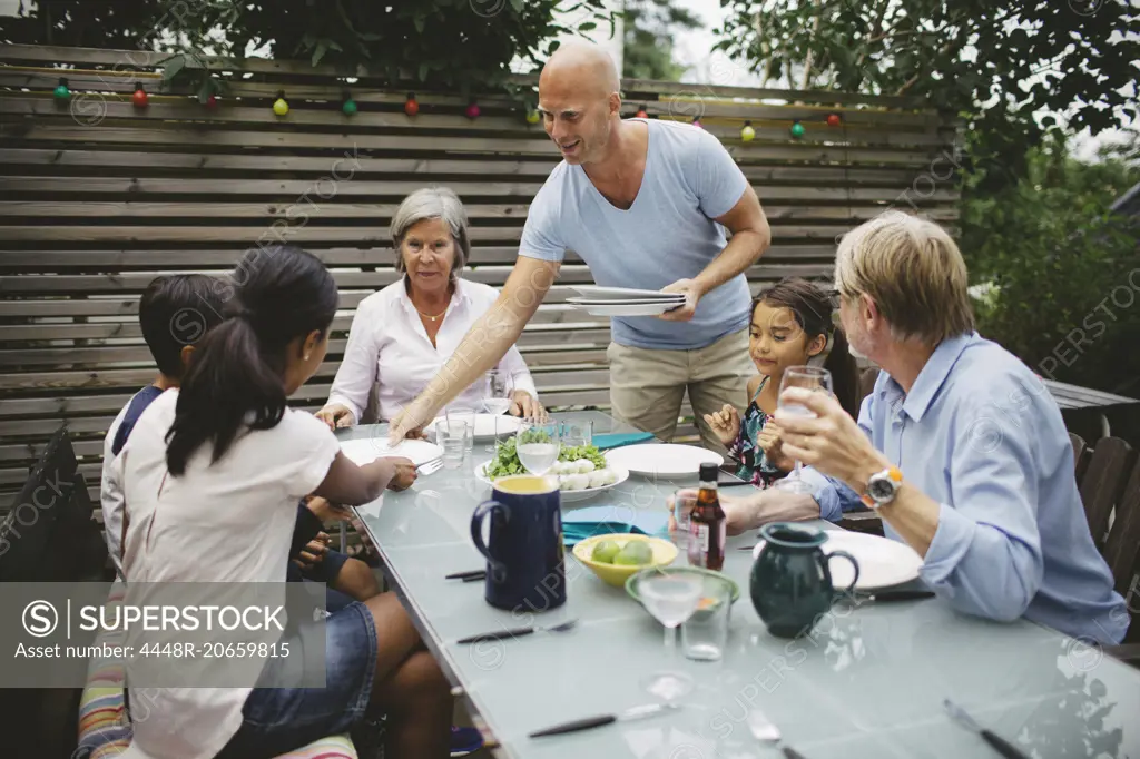 Man serving food to family at outdoor dining table