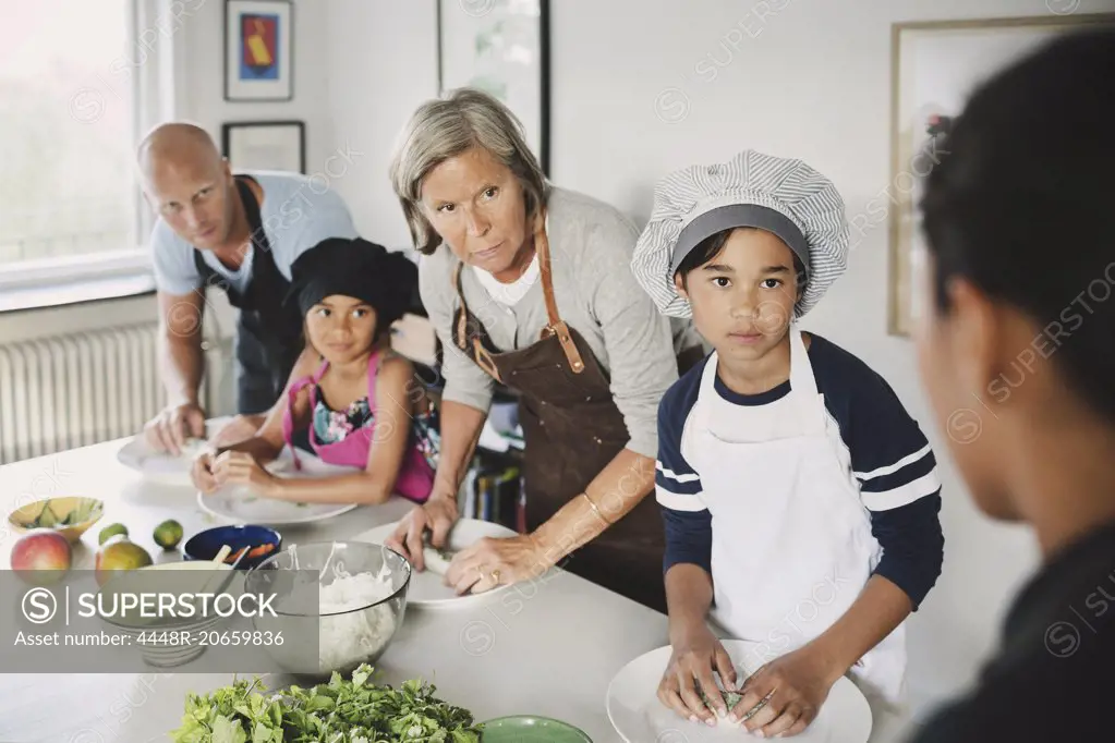 Family looking at woman while preparing food in kitchen