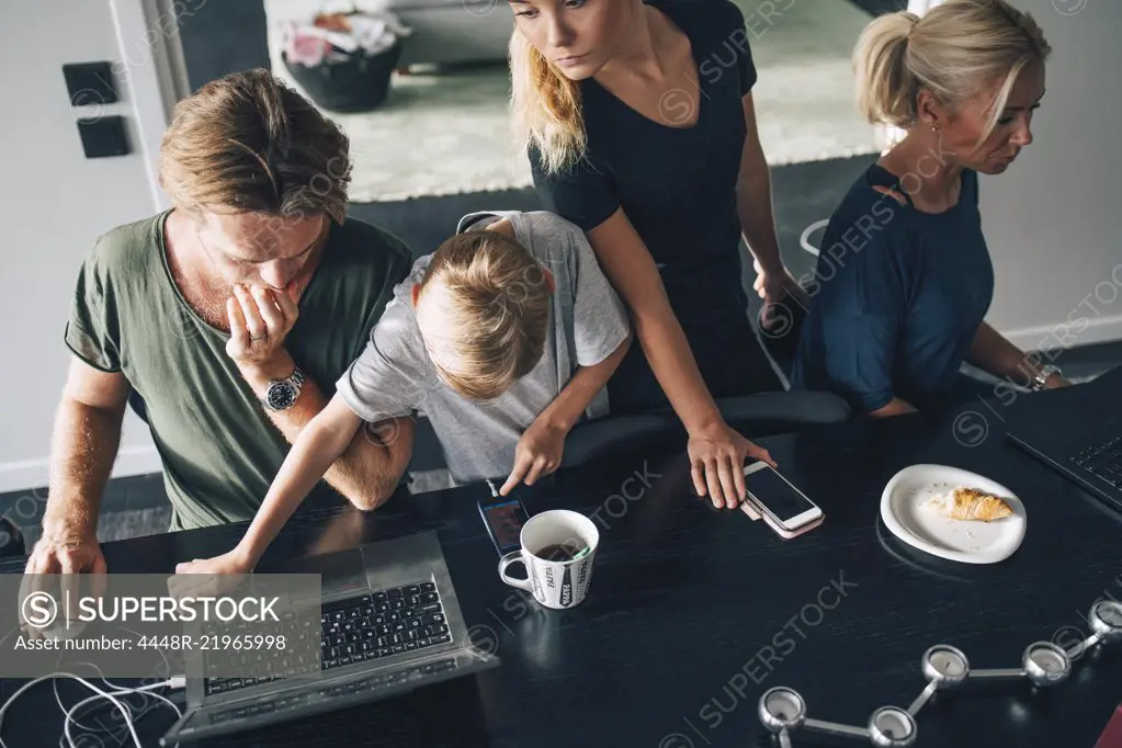 High angle view of family using technologies at dining table in room