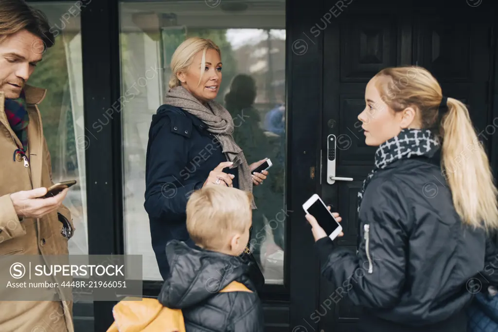 Family standing with mobile phones by house door