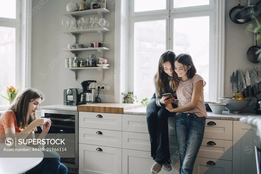 Female friends using mobile phone in kitchen at home