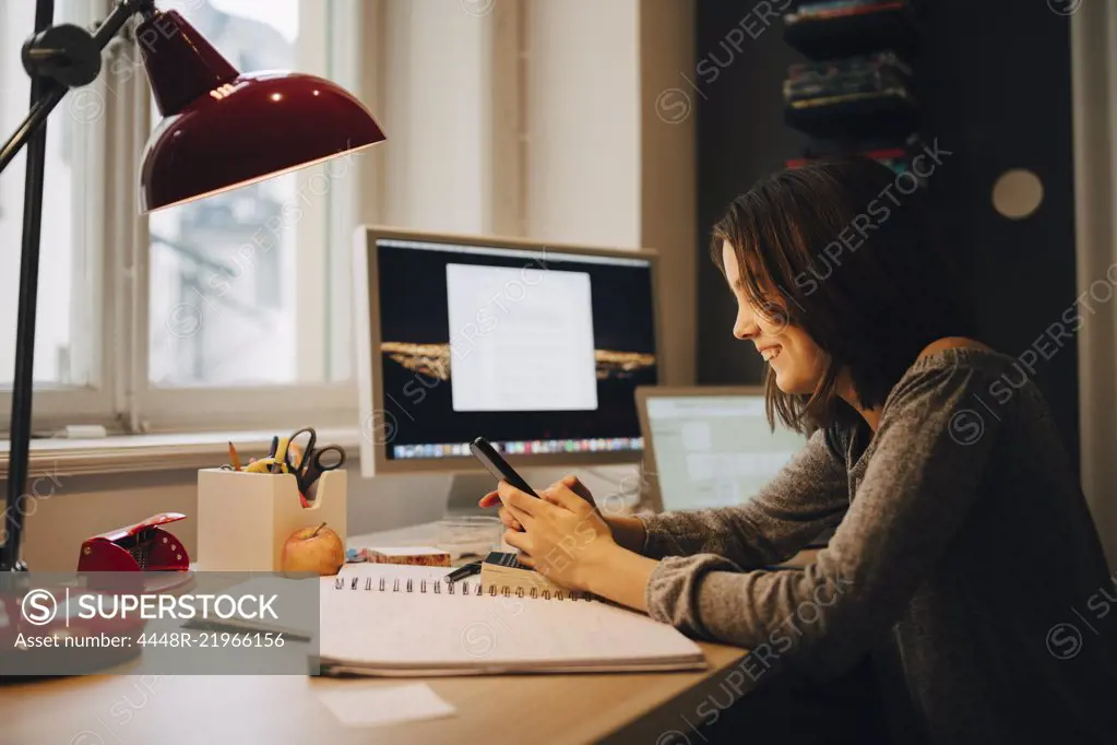 Happy girl using mobile phone while sitting at illuminated desk