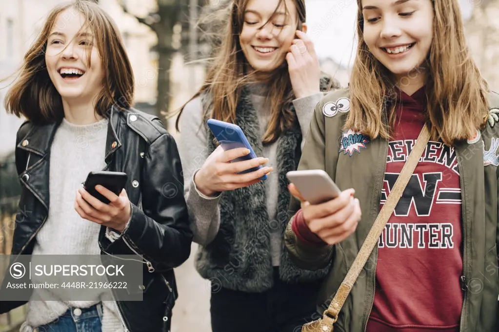 Midsection of female friends using mobile phone while walking in city