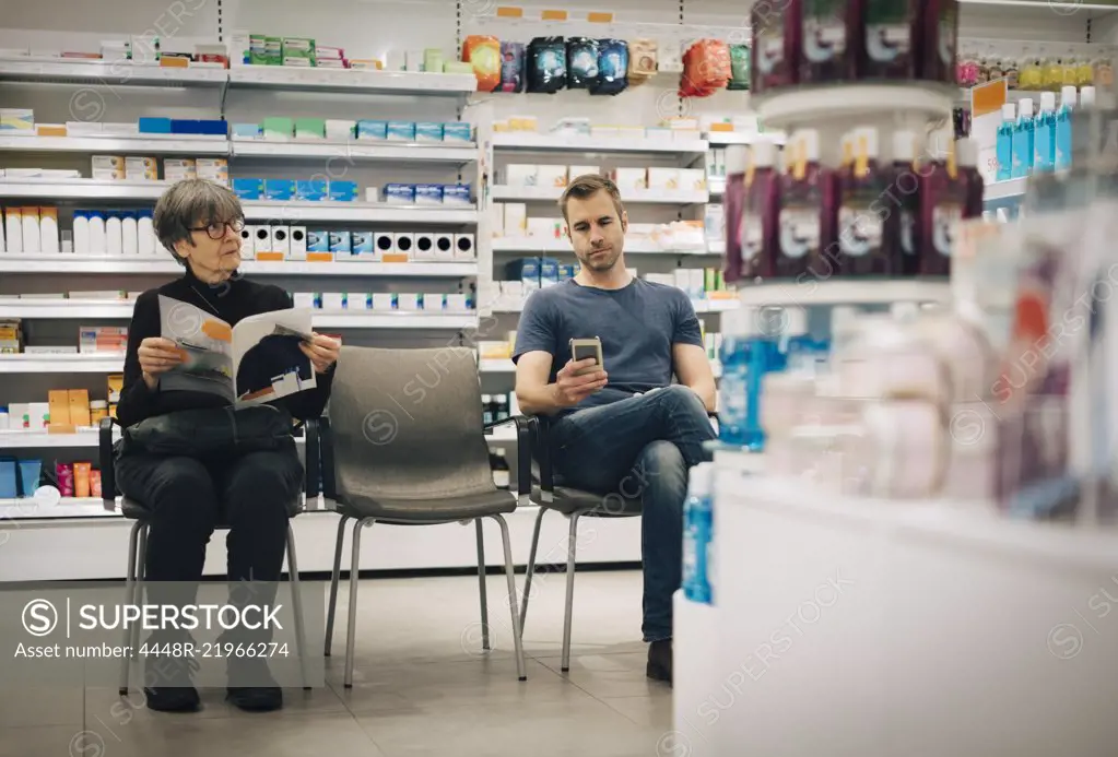 Customers sitting on chairs against medicine rack at pharmacy store