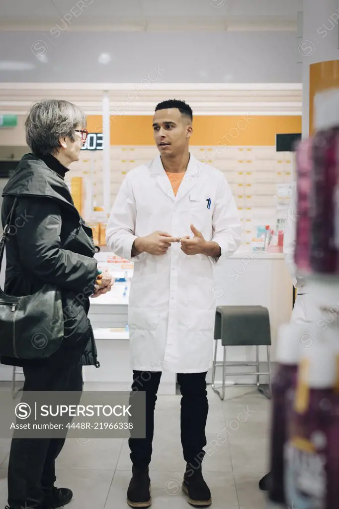 Full length of male pharmacist talking with senior female customer in medical store