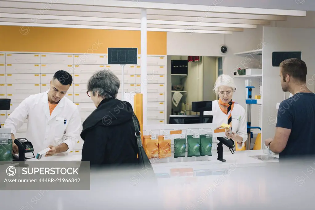 Rear view of customers buying medicines from pharmacists at checkout in store