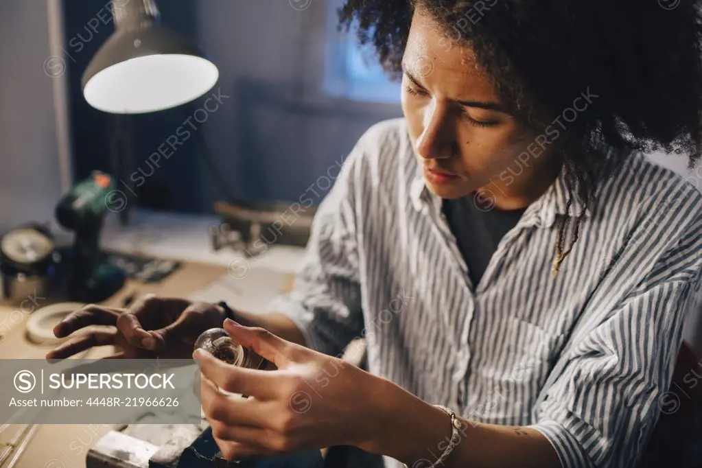 Young man making equipment at illuminated desk in workshop