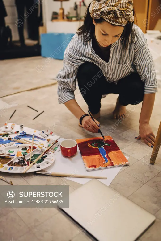 Female artist painting on paper while crouching at art studio