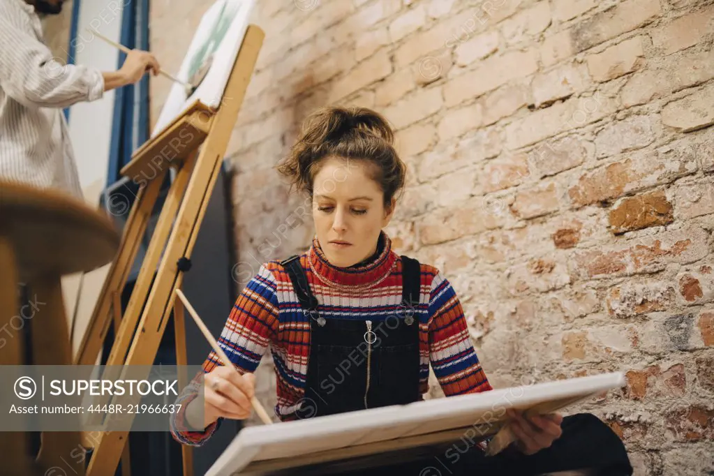 Low angle view of female and male artists painting on canvas at art studio