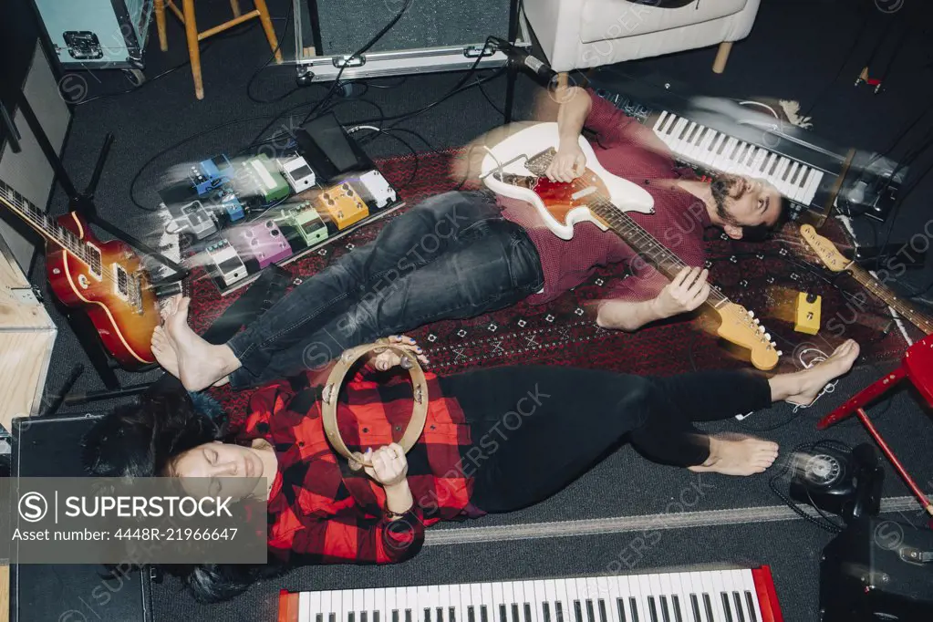 High angle view of male and female friends playing instruments while lying on floor at studio