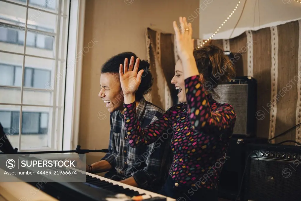 Happy friends enjoying while playing piano and practicing at recording studio