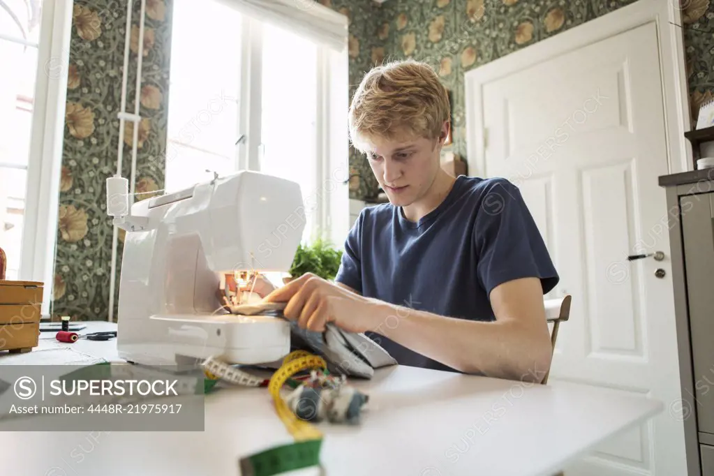 Young man sewing textile at home