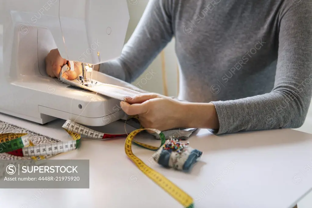 Midsection of teenage girl sewing textile at home