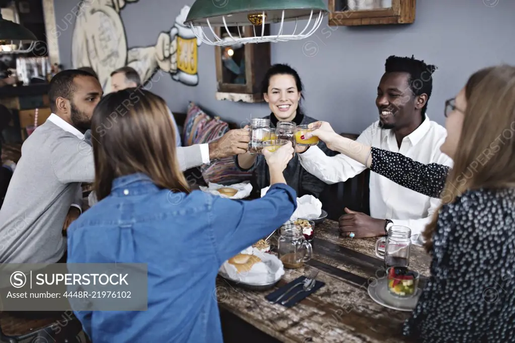 Happy friends toasting drink while sitting at dining table in restaurant