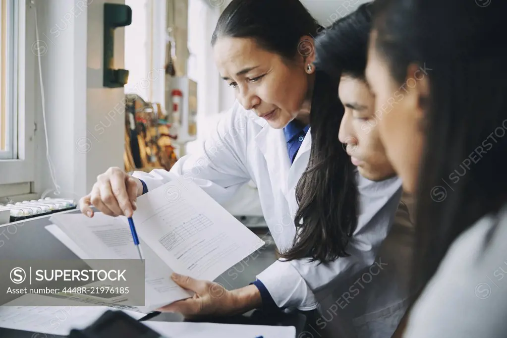 Teacher pointing at book to young engineering students in university classroom