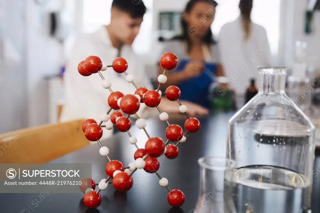 Molecular structure by glassware on table against young students in chemistry laboratory