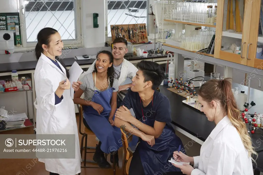 Happy mature teacher explaining to young multi-ethnic university students sitting in chemistry laboratory