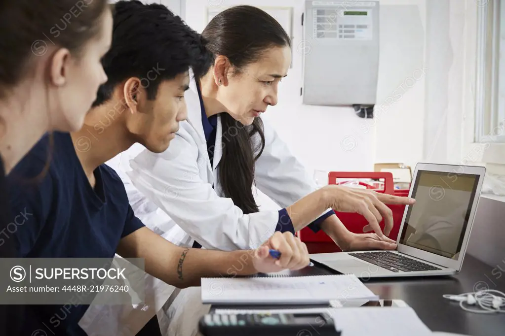 Teacher pointing at laptop screen to young engineering students in classroom