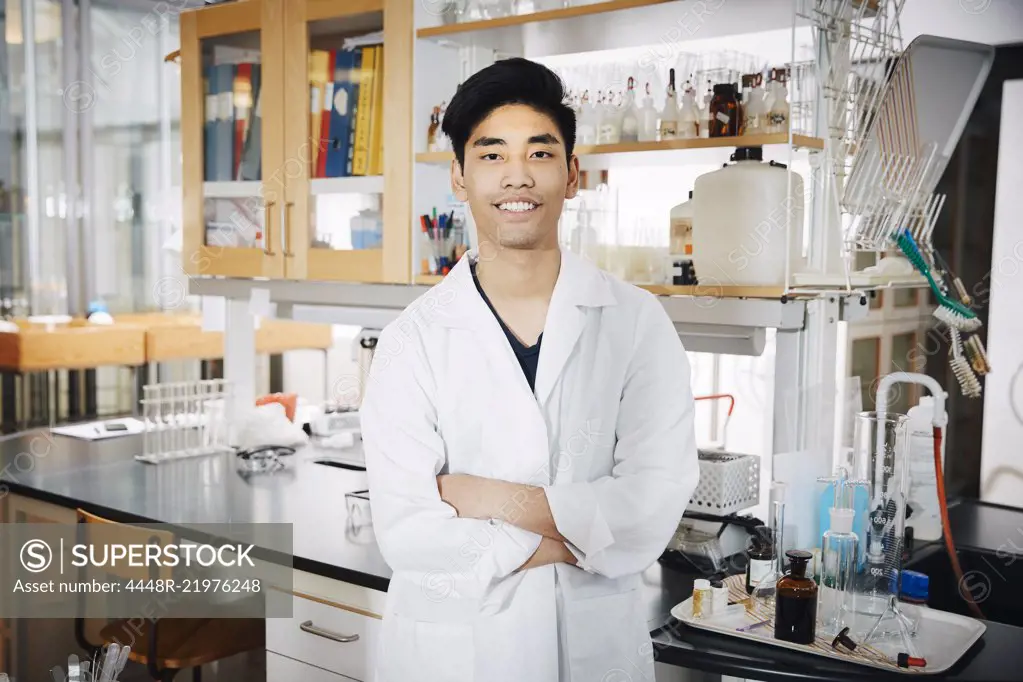 Portrait of confident young male university student standing with arms crossed at chemistry laboratory